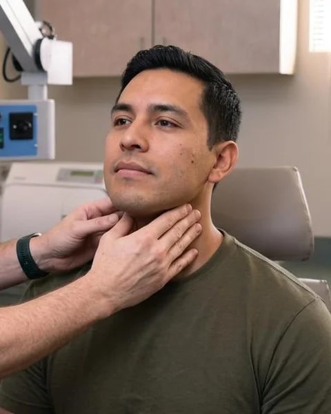A seated patient having his neck examined